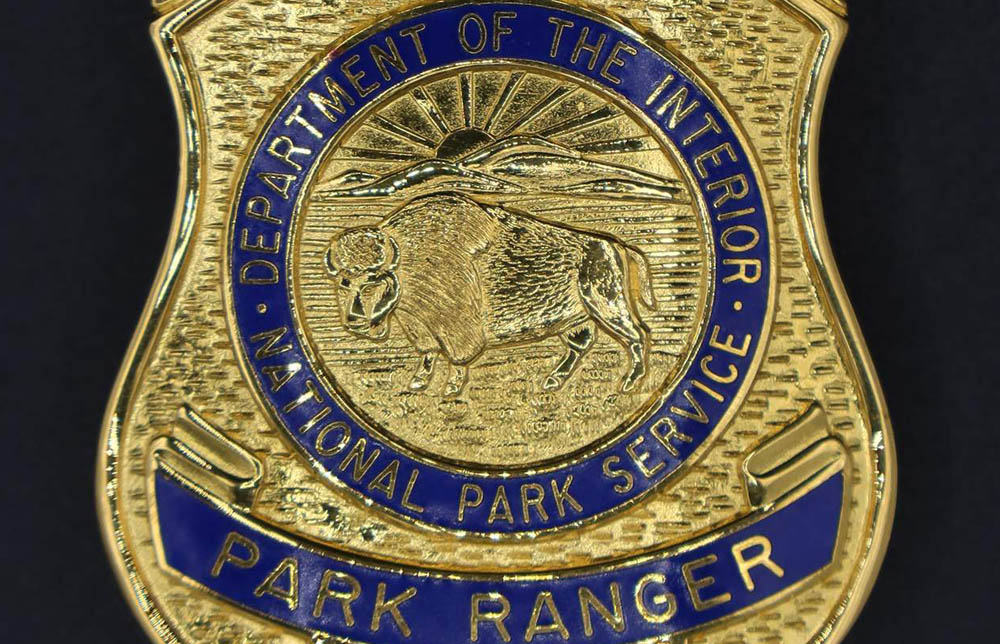 Gold shield-shaped badge with eagle on top. Marked U.S. Park Ranger and 1 in blue. Round seal has blue border with bison in the middle. 
