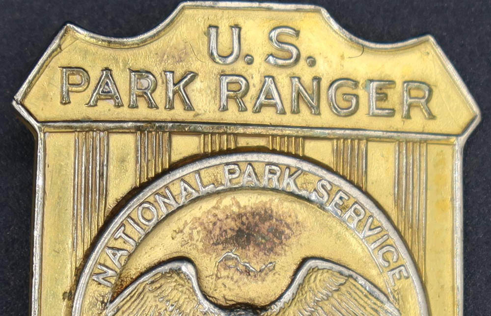 Gold shield-shaped badge marked U.S. Park Ranger. The raised round seal in the middle has an eagle looking to its left.