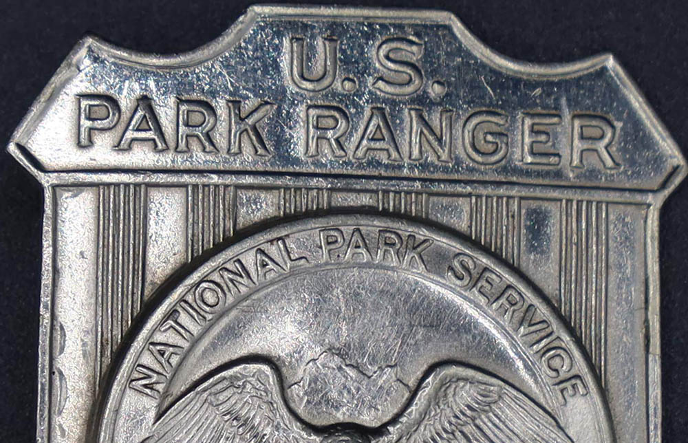 Silver shield-shaped badge marked U.S. Park Ranger. The raised round seal in the middle has an eagle looking to its left.