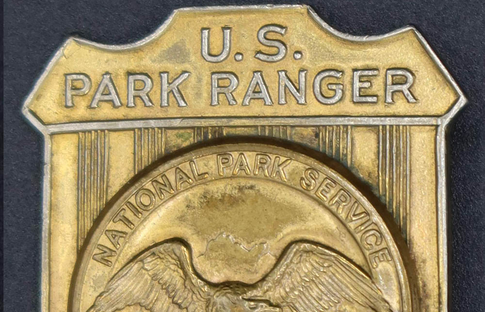 Gold shield-shaped badge marked U.S. Park Ranger. The raised round seal in the middle has an eagle looking to its left.