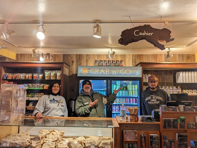 Three staff members smile behind a counter with food items