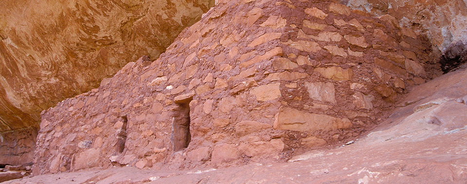 a stone structure with two doors sits beneath a rock overhang a stone structure with two doors sits beneath a rock overhang