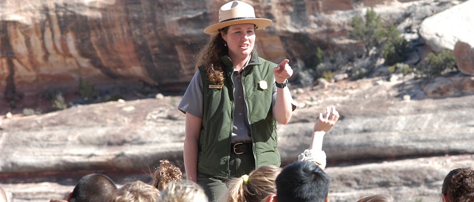 a park ranger points while children in the foreground raise their hands