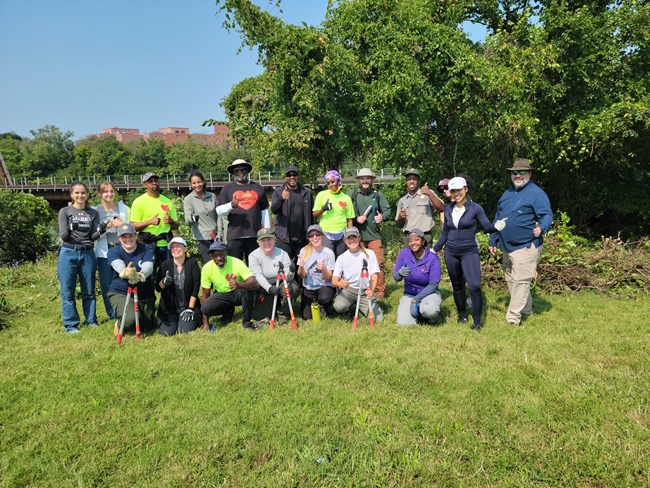 A group of people standing in front of trees and a river.