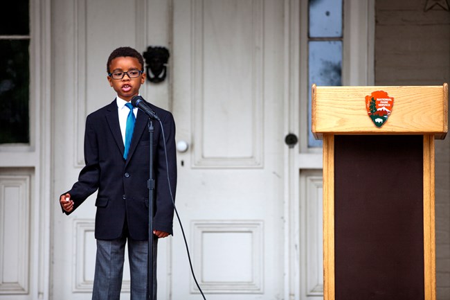 a young boy in a suit recites a speech