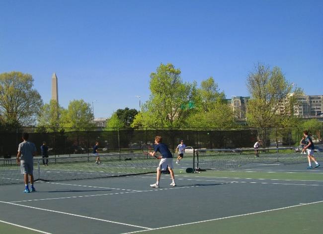 Tennis players at the East Potomac Tennis Center Several tennis students playing tennis on an outdoor tennis court. The Washington Monument is in the background.
