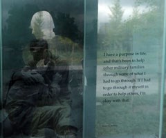 Etched engraved writing on glass and reflection of trees next to bronze relief cut out of soldier