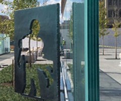 Large bronze cutouts of solders next to glass with grass underneath it