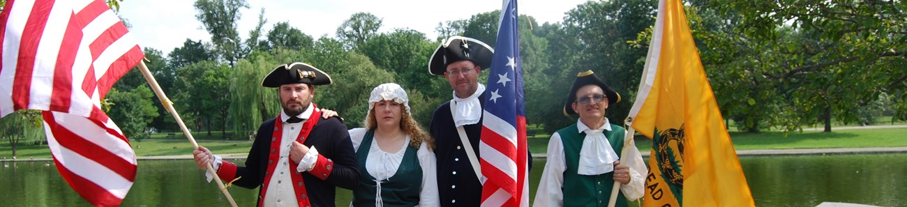 Four colonial era reenactors holding flags