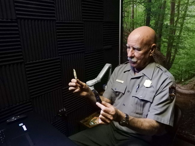 A park ranger holding up American Indian arrowheads to a screen as a part of a distance learning program