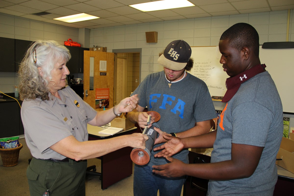 Two high school students examining a grey cylinder with a park ranger.