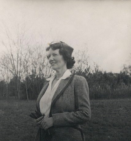 A woman stands in the forefront in a jacket in a field.