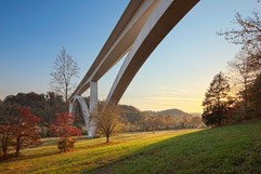 NPS Photo/Copyright Marc Muench White arched bridge spanning valley with grass and trees in fall