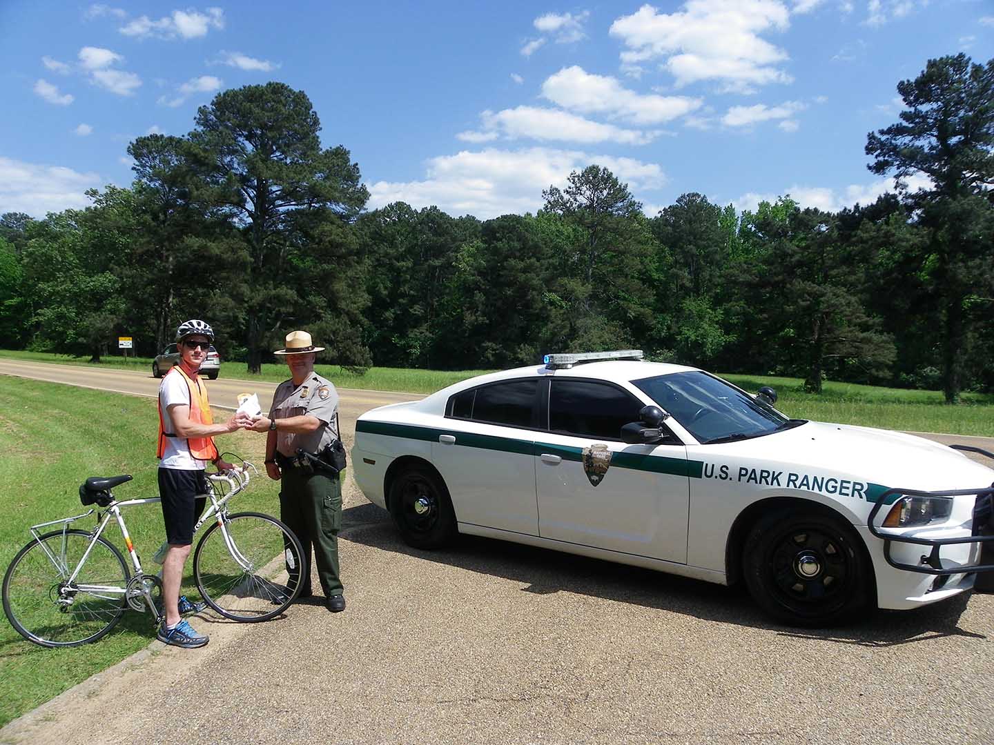 bicyclist, ranger, and patrol vehicle next to roadway