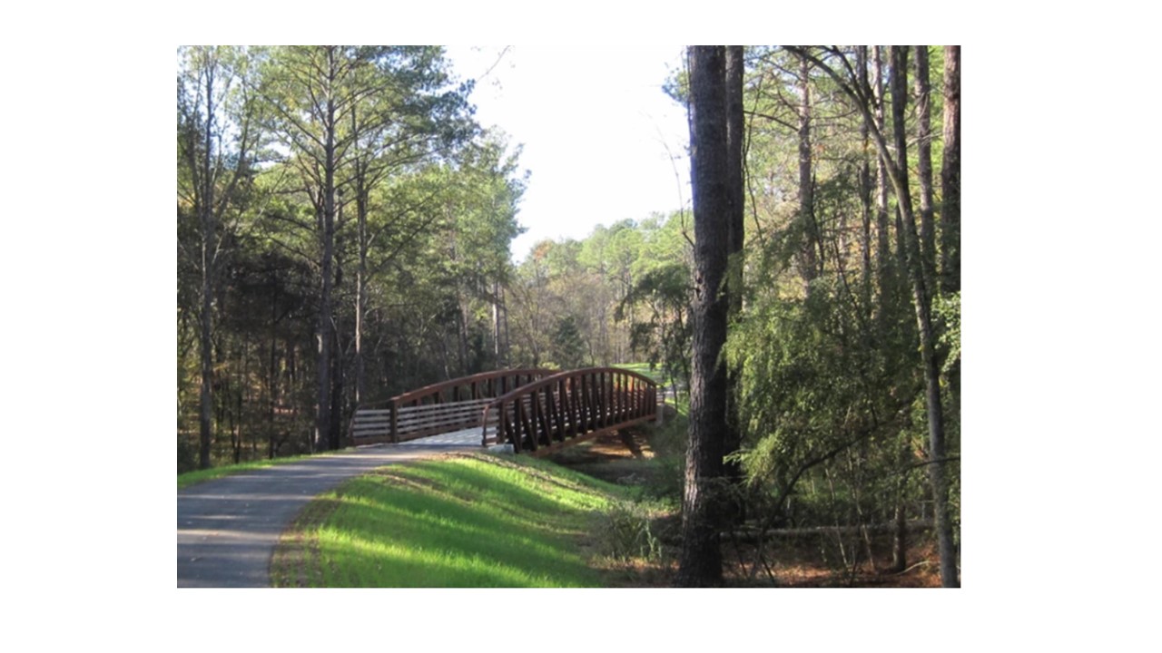A paved treelined trail with a bridge spanning a dry creek bed. The trail is free of walkers.