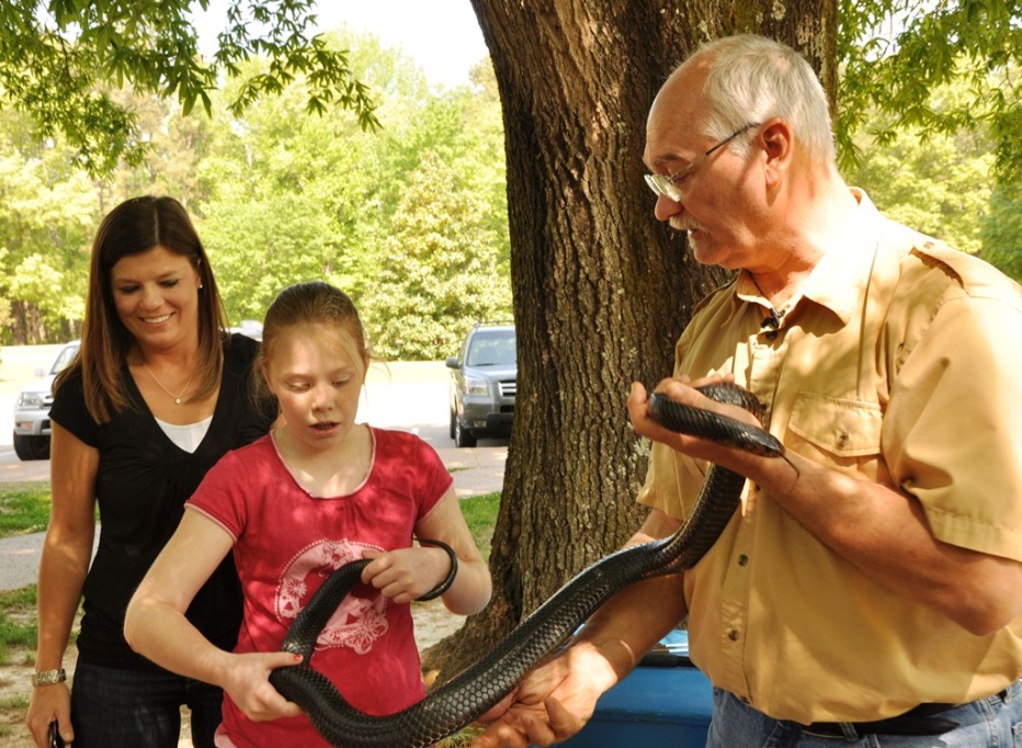 A volunteer handles a live snake as he shows it to a child and adult visitor
