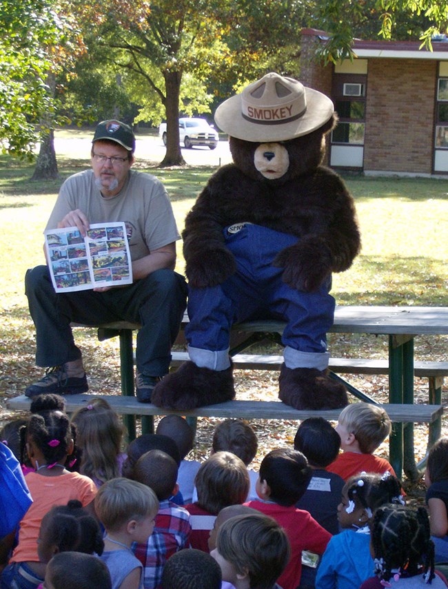 A fire fighter and Smokey Bear teach children about wildland fire