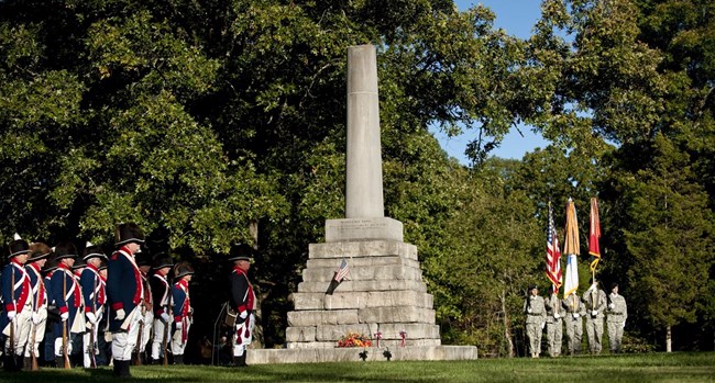 People dressed in revolutionary war period costumes stand by the memorial for Meriwether Lewis.