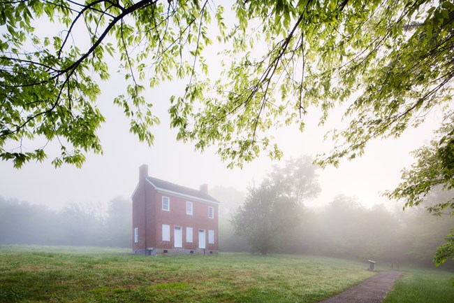 Brick two story home with white doors and shutters in the fog. Grass surround the home