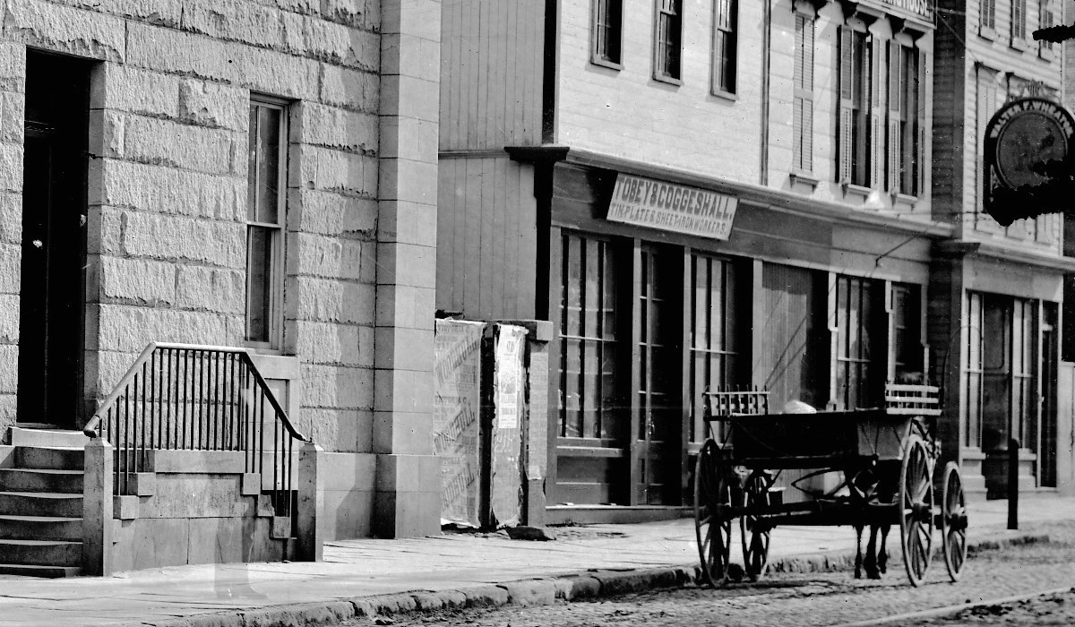 Black and white photo depicts a wagon on the street in front of Tobey & Coggeshall storefront.