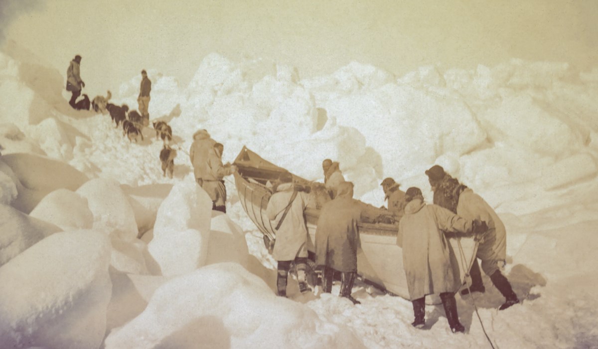 Men push canoe through ice and snow.