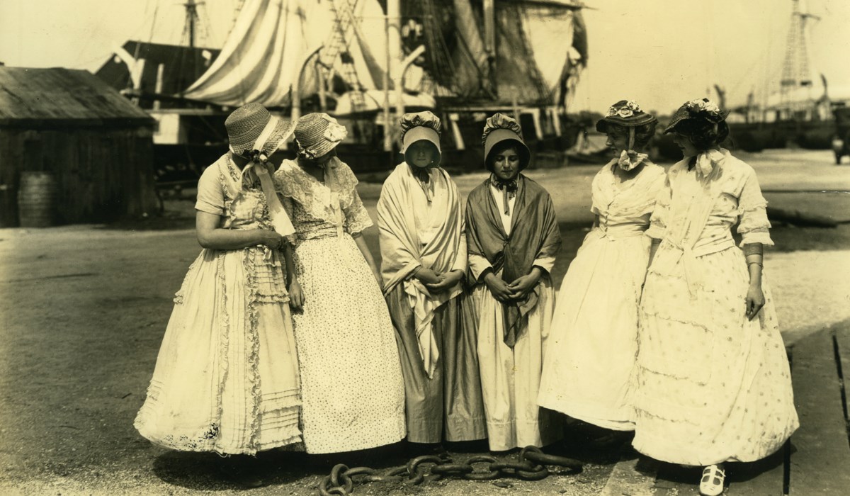 Sepia image of six women, gathered at docks in front of ships.