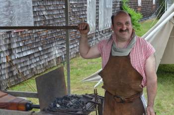 burly man stands next to a forge