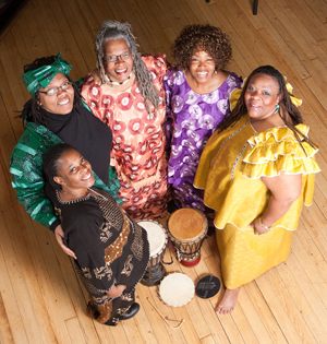 Nzinga's Daughters circle around a drum in traditional clothing.