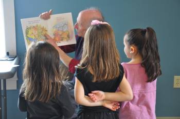 man reads a book to three young children