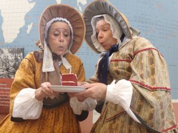 Ruth and Abby, the park's 1850s ladies two women in 1850s garb hold a slice of cake and blow out the candle