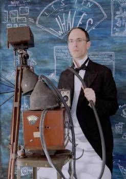 Listen to the Whales man standing next to strange looking, old contraption