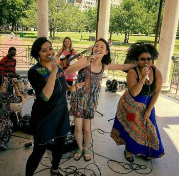 young men and women of various ethnic races and backgrounds playing music and singing joyously in an outdoor park setting