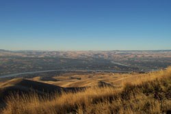 A grassy hillside overlook where two rivers intersect down below on a sunny day.