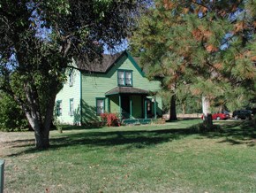 A green two story house in the distance blocked by several trees.