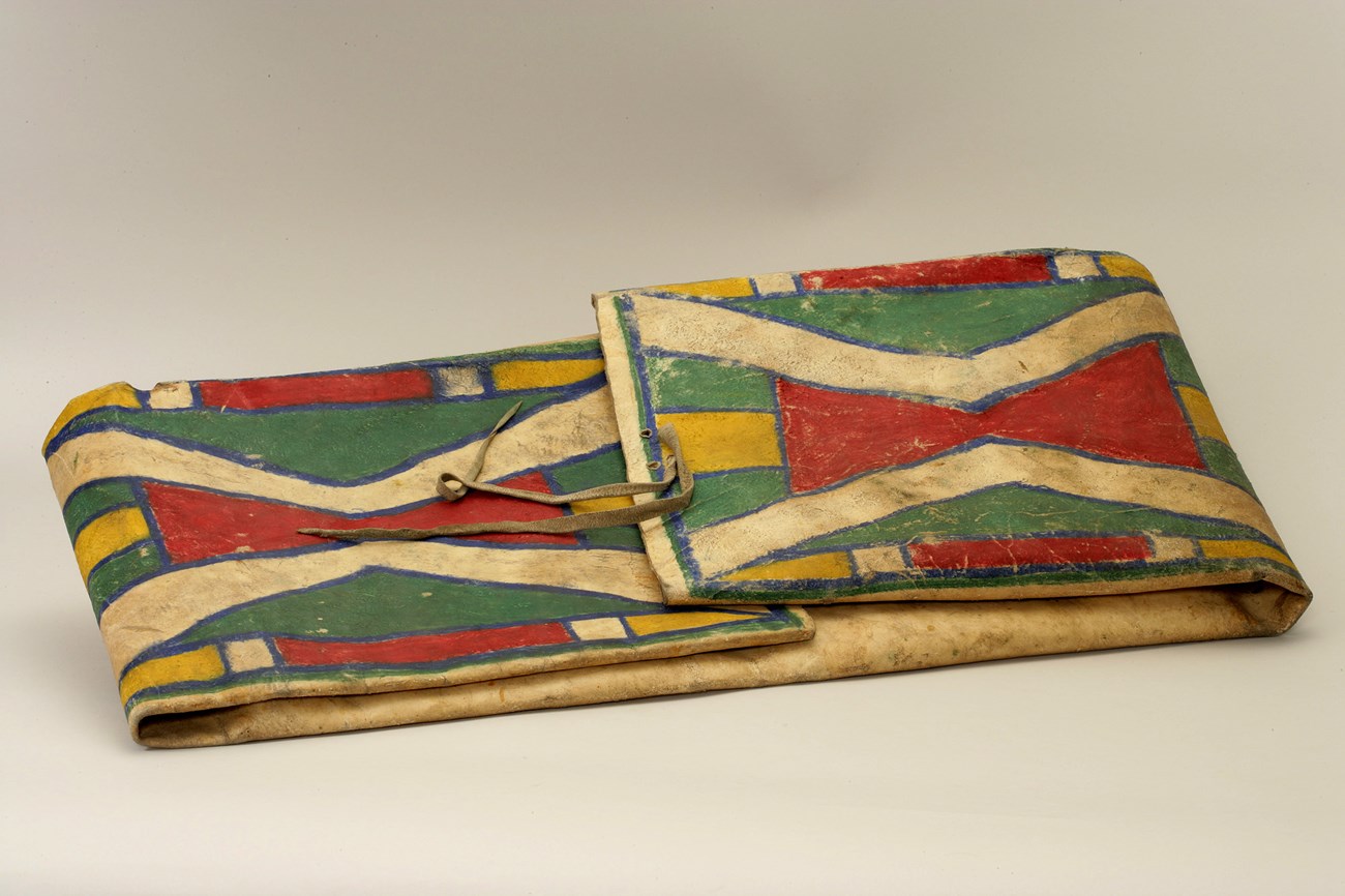 Raw hide folded into a rectangle with flaps for it to be opened for storage. The top is painted with colorful geometric designs.