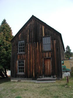A tree stands next to a two story building with old wood paneling.