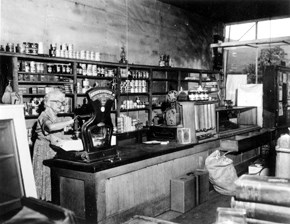 A women in a store measuring a package with shelves of merchandise behind her.