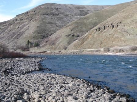 A river with a rocky beach and the mountains in the background.