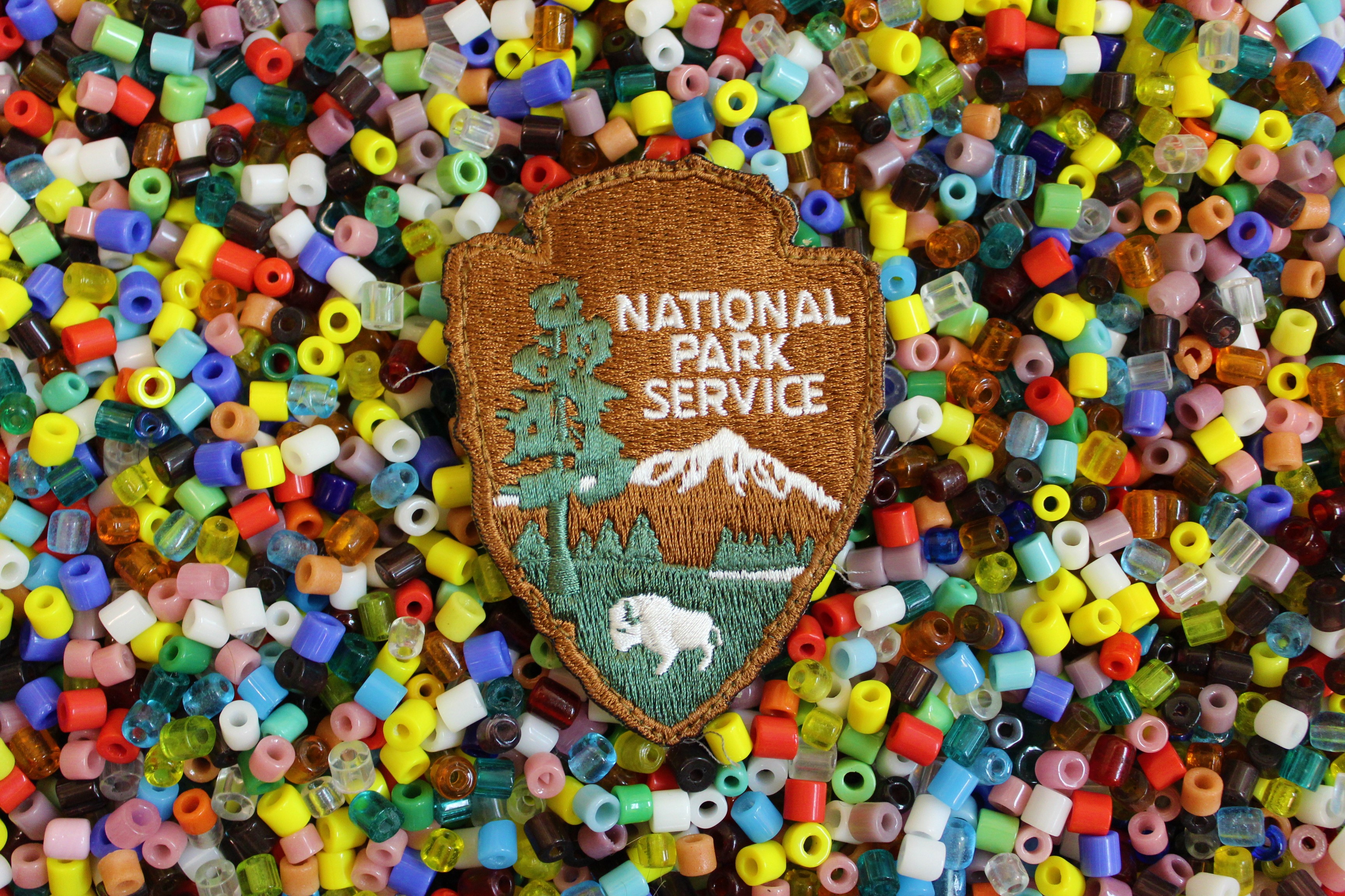 A National Park Service arrowhead badge laying on top of an array of colorful beads