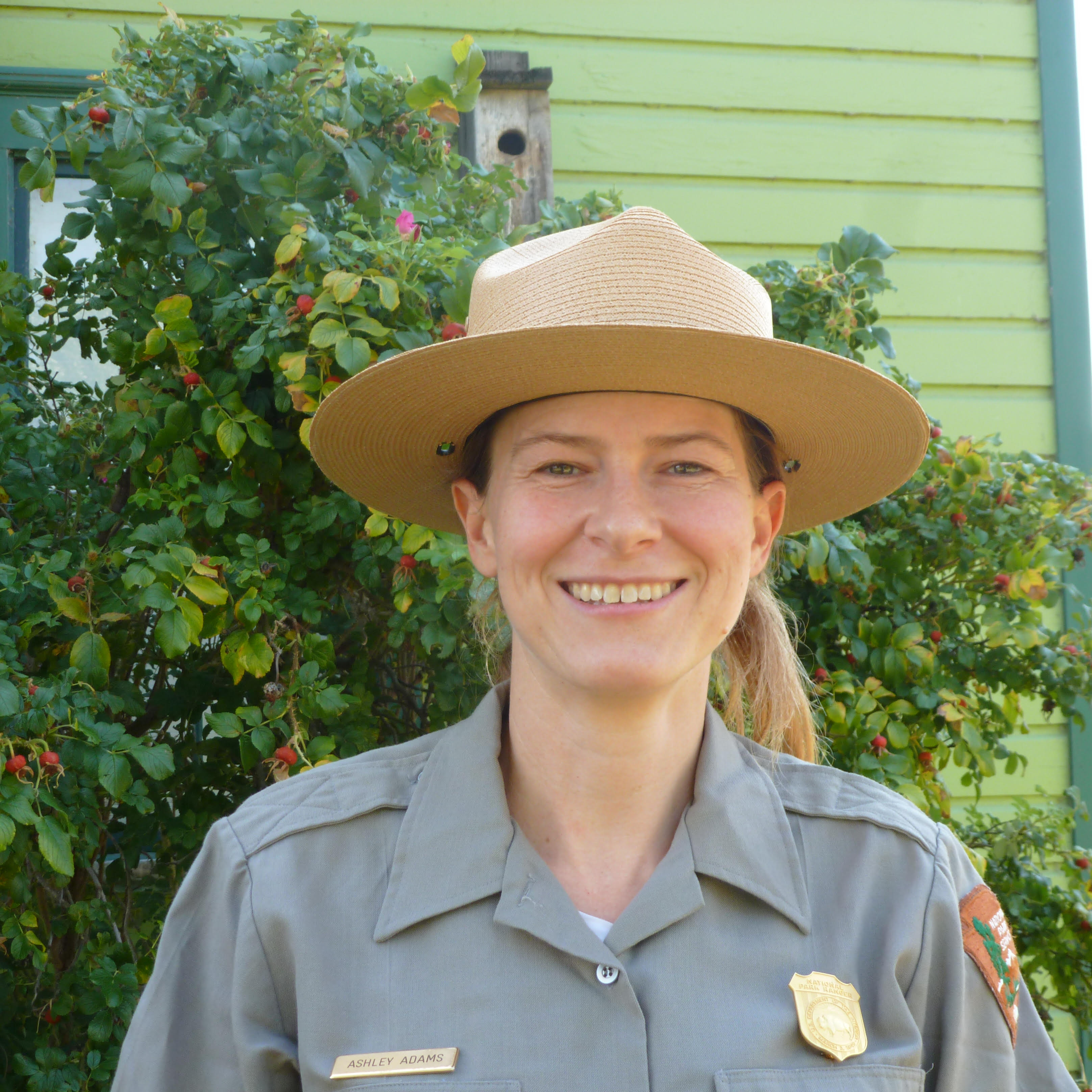 Female park ranger standing in front of rose bush, smiling.