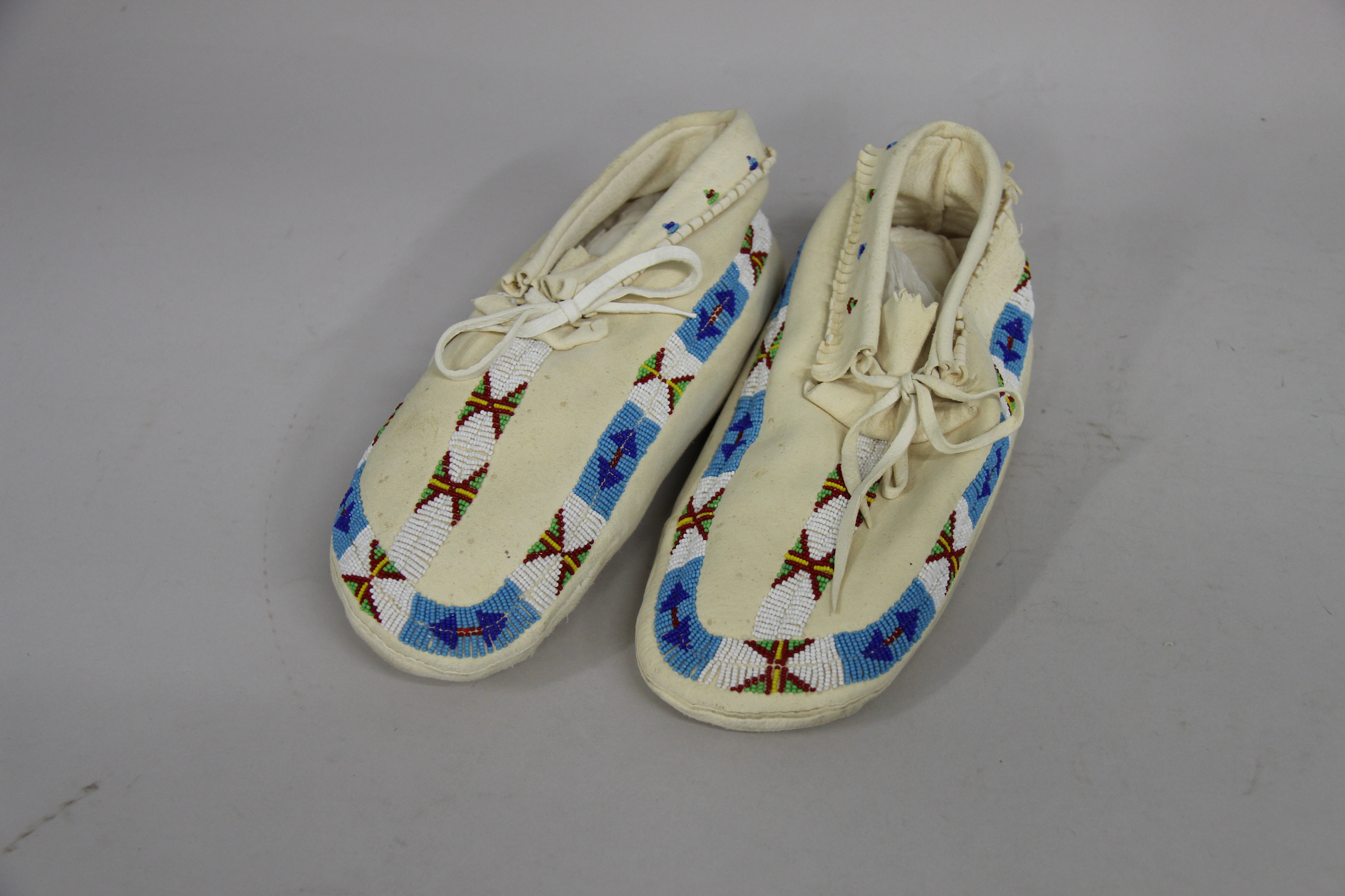 Light buckskin moccasins with a blue, white, red green, and yellow bead pattern around edge.