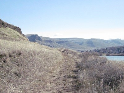 A hiking trail on a grassy hillside with a river in the background.