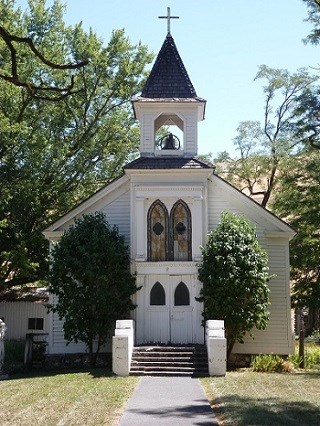 A white church with two large trees by the church doors on a sunny day.