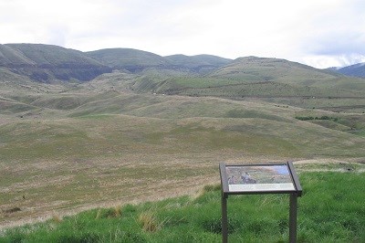 Vista of rolling hills and canyons with a wayside panel explaining the battle in the foreground.