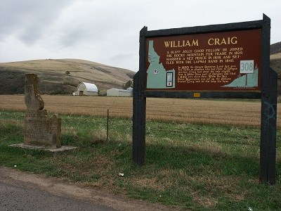 A dark brown sign with the words 'William Craig' on it next to a monument shaped like the state of Idaho.