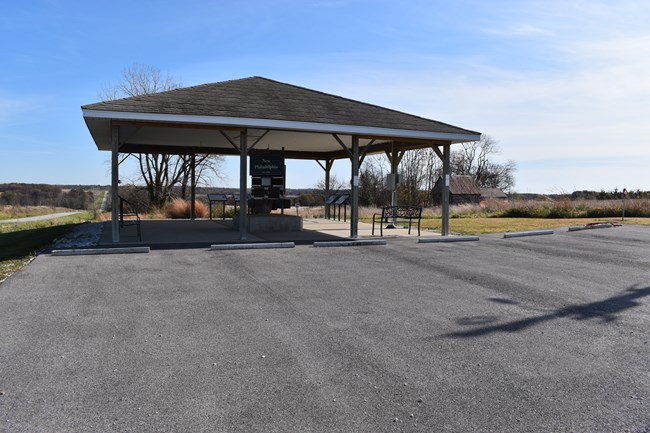 An asphalt parking lot in front of a large, open-sided kiosk with informational signs.