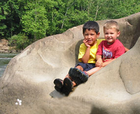 Two boys sitting in river sculpted rock on river bank