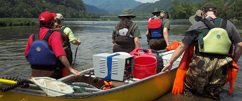 volunteers pushing a canoe with equipment in a river