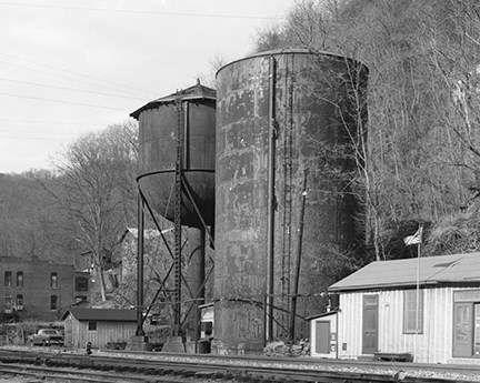 Two large steel water tanks one a tall column and one elevated sitting next to railroad tracks