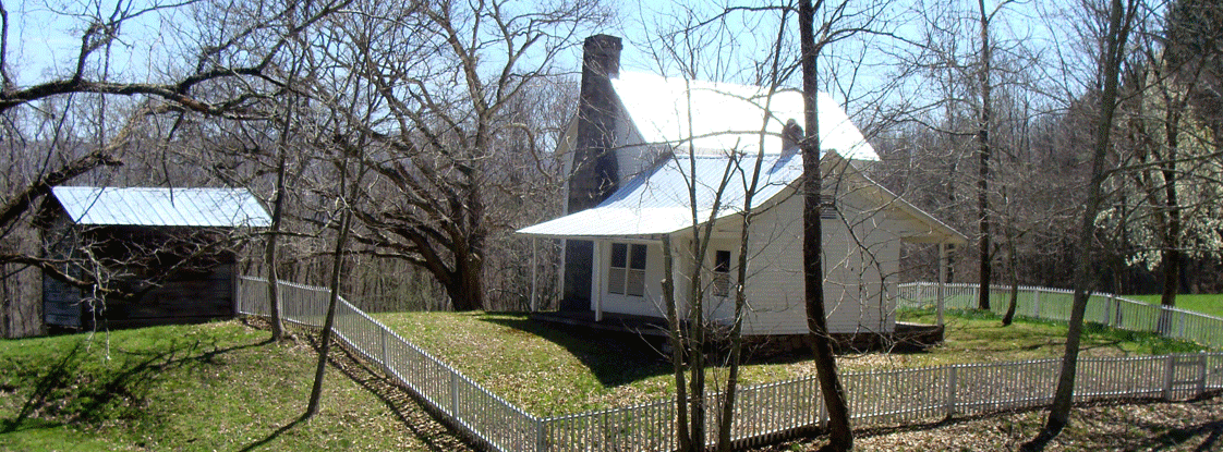 A white house surrounded by a simple wooden fence in a grassy field with a few trees.